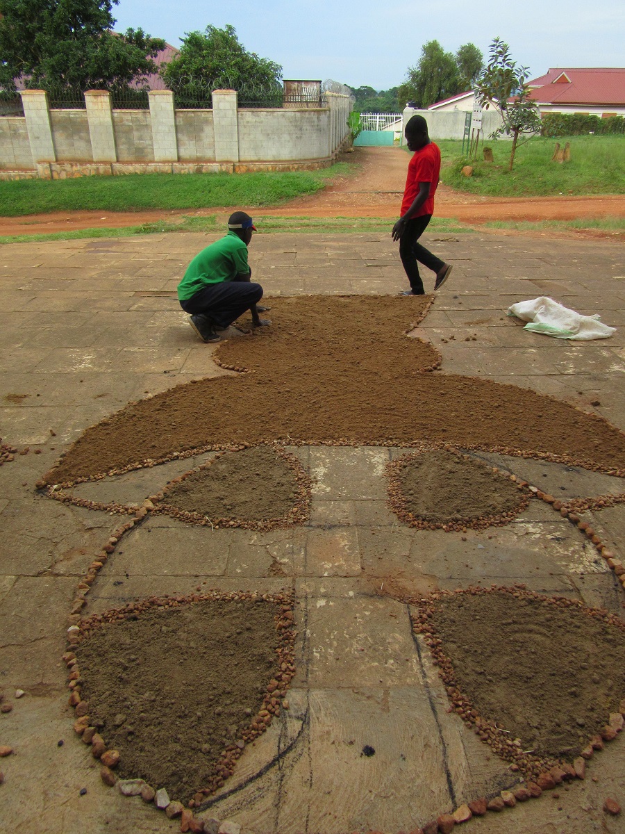 Two male teens working on large, sand and stone image.